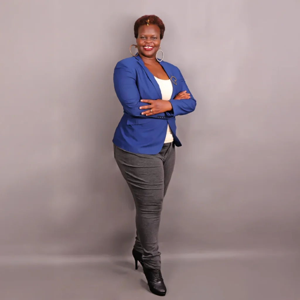 Beverley in a dark blue blazer, white top, gray pants, and black boots.